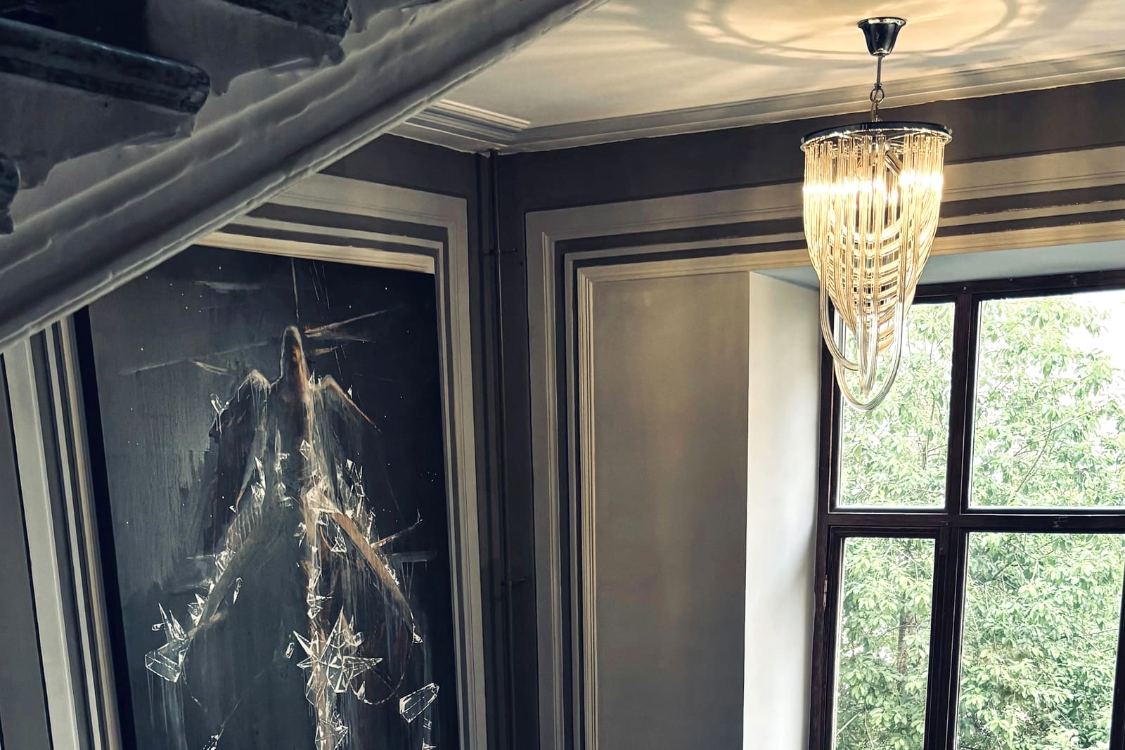 A quiet panelled room with tall windows and a chandelier, light falling through the glass.