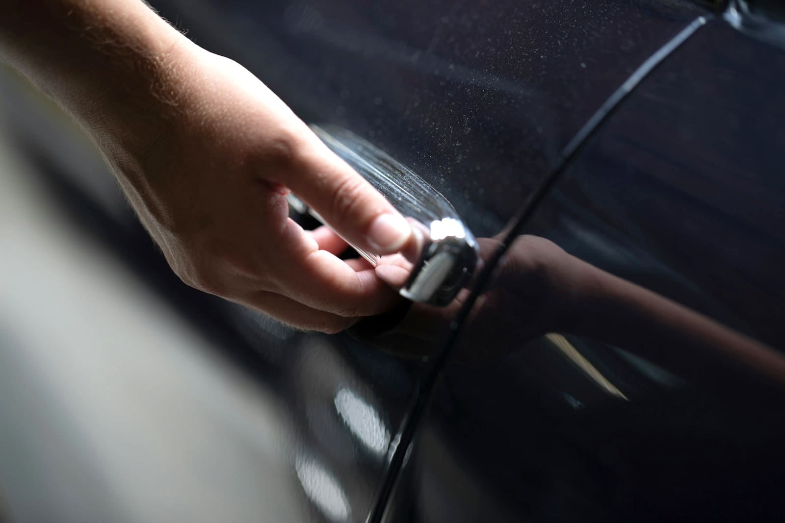 A hand resting on the door handle of a dark car, about to open it.