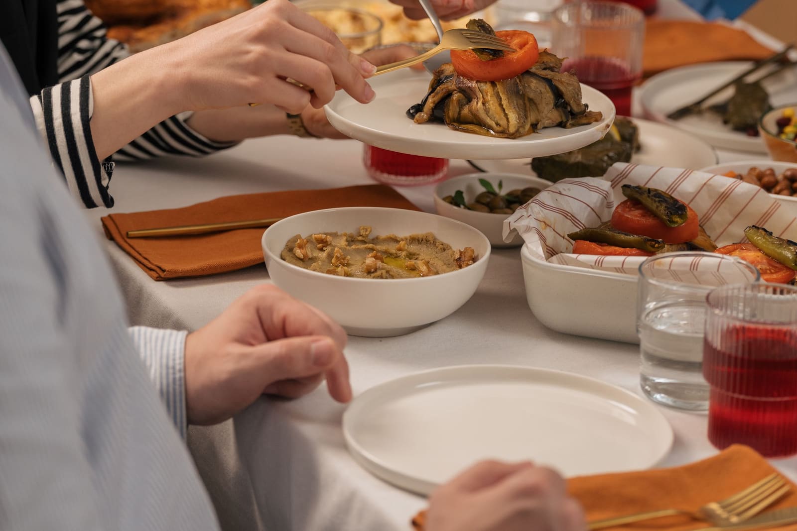 Hands serving from shared dishes at a table laid for a family meal.