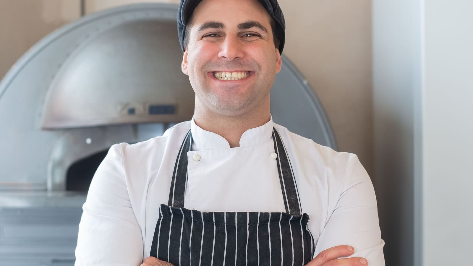 A chef in an apron standing in his kitchen, arms folded, looking straight at the camera.