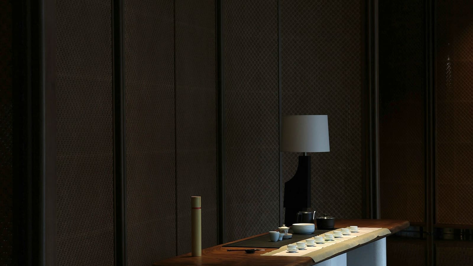 A single lamp lighting a low table laid for tea in a dark panelled room.