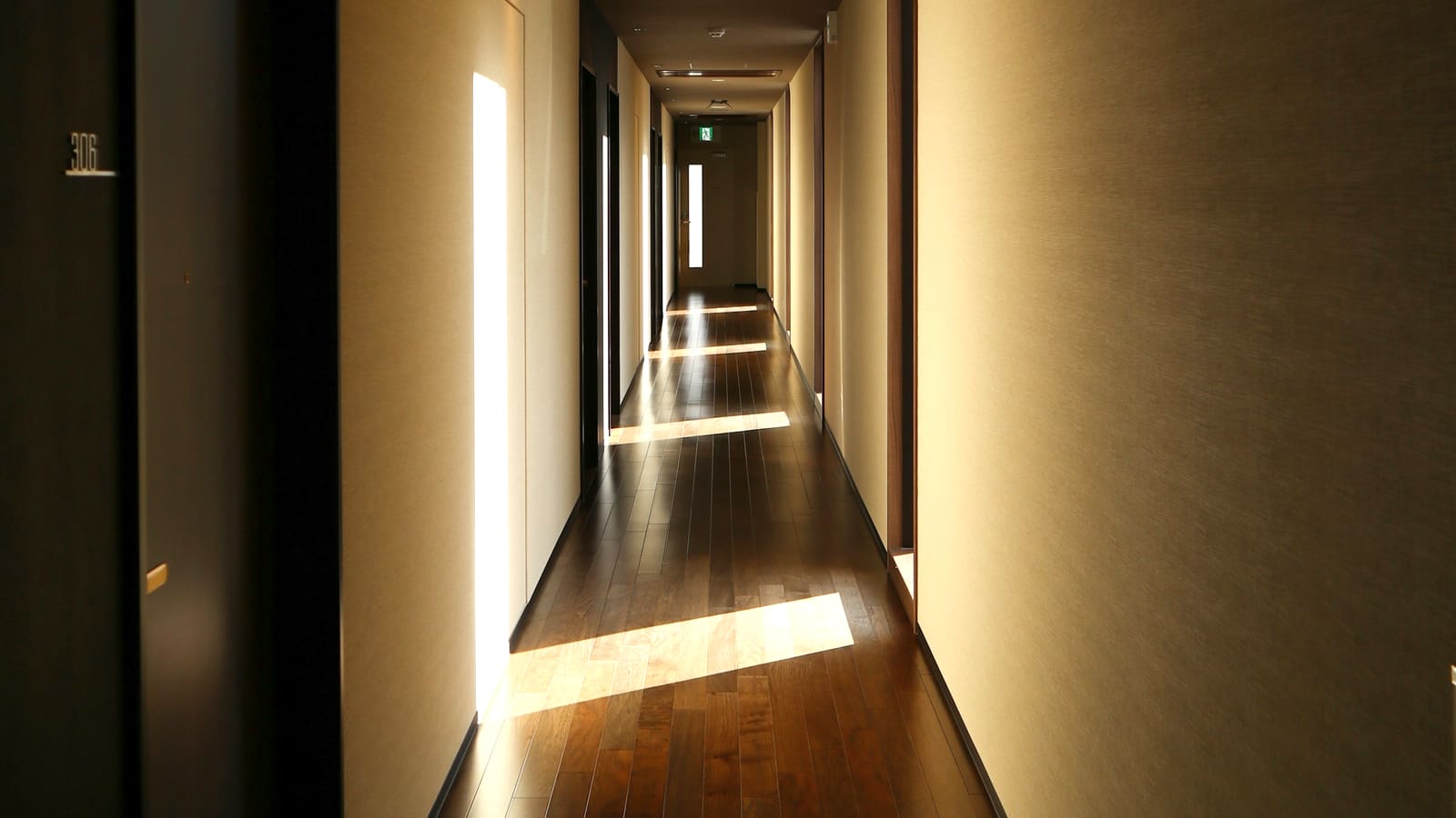 A softly lit private hallway receding into shadow, daylight falling across the floor.