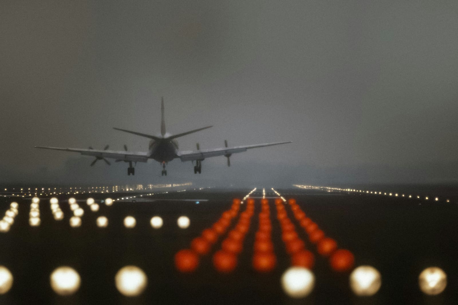 An aircraft on final approach at dusk, runway lights burning in a line beneath it.